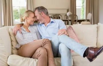 Older man and younger woman couple sharing a romantic moment on the living room couch.
