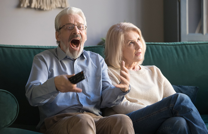 Excited older man enjoys watching the TV while his mature wife gets annoyed