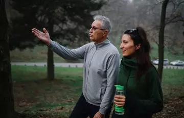 Older man directs his younger girlfriend on a walk through the park
