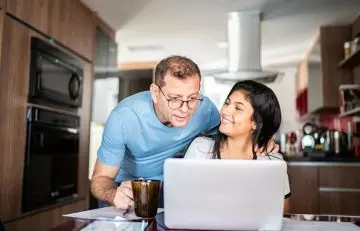 Older man helps younger woman using a laptop at the dining table