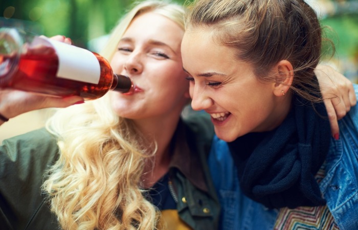 A woman drinking wine while having fun with her female friend