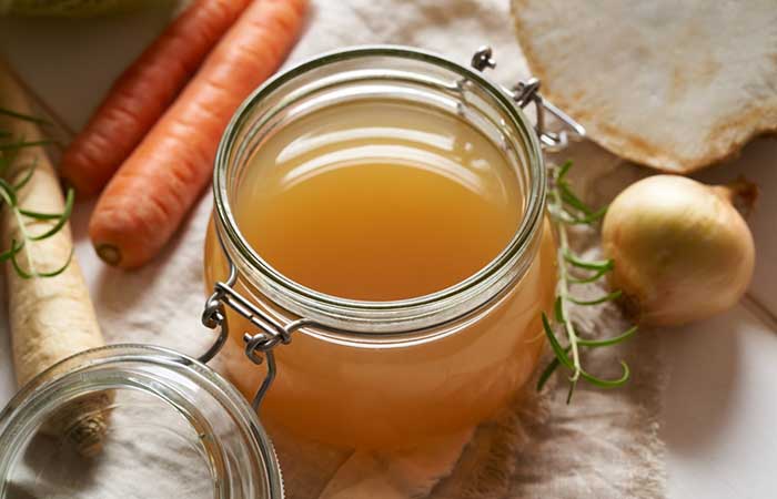 Homemade beef bone broth in a glass jar, with carrots, celery root and other fresh vegetables