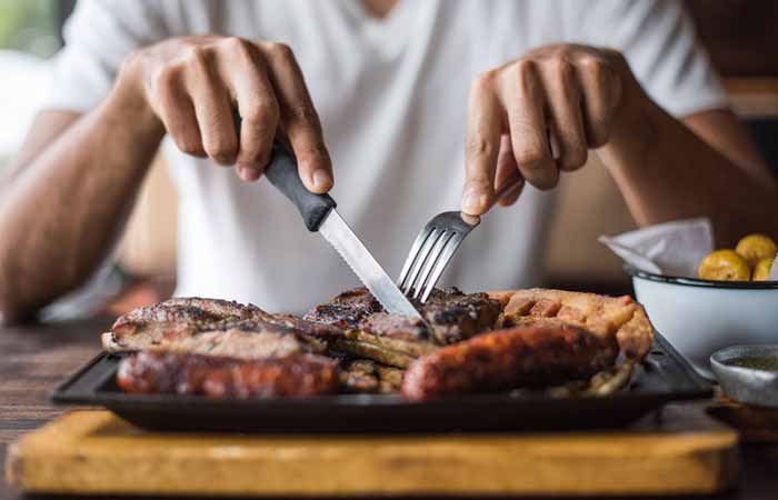 Close-up of hands slicing steak using fork and knife