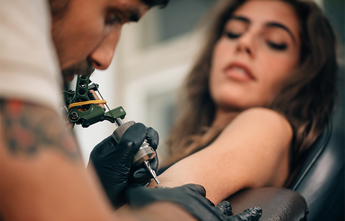 A closeup of a skilled tattoo artist inking a client’s upper arm during a tattoo session.