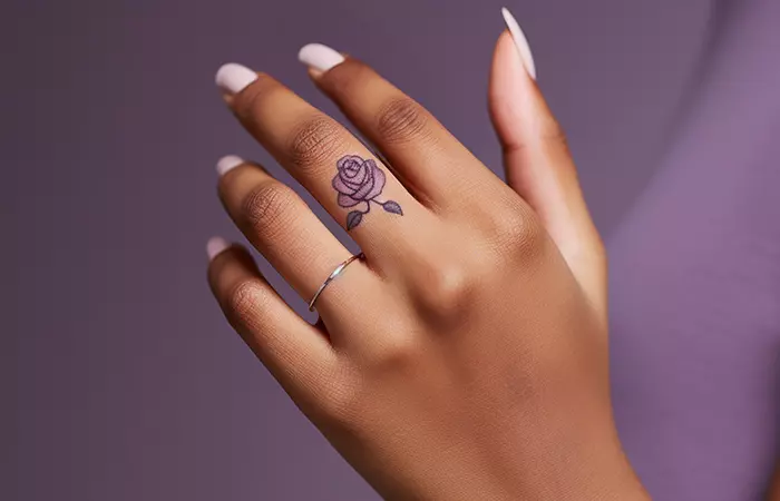 A minimal purple rose tattoo on the finger