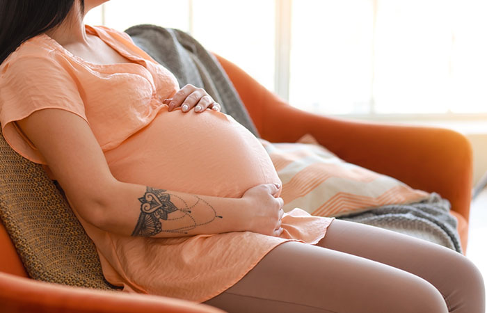 A pregnant woman with a tattoo on her forearm resting on a sofa.