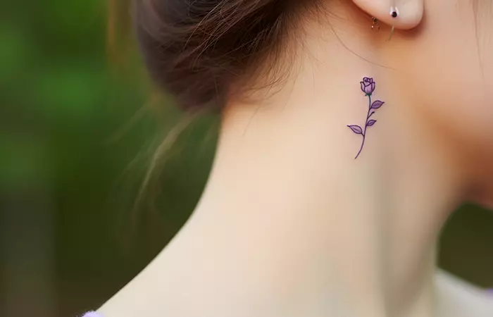 A simplistic purple rose tattoo under the ear