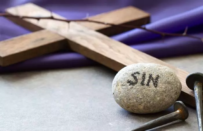 A stone with the word ‘sin’ written on it, lying beside a wooden cross.