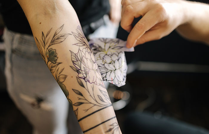 A tattoo artist applying a tattoo stencil on the forearm of a client.