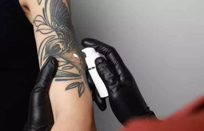 A tattoo artist holds a client’s forearm in order to moisturize a fresh tattoo.