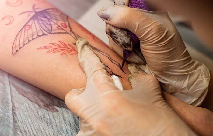 A tattoo artist holds the forearm of a client for a cover-up tattoo session in progress.