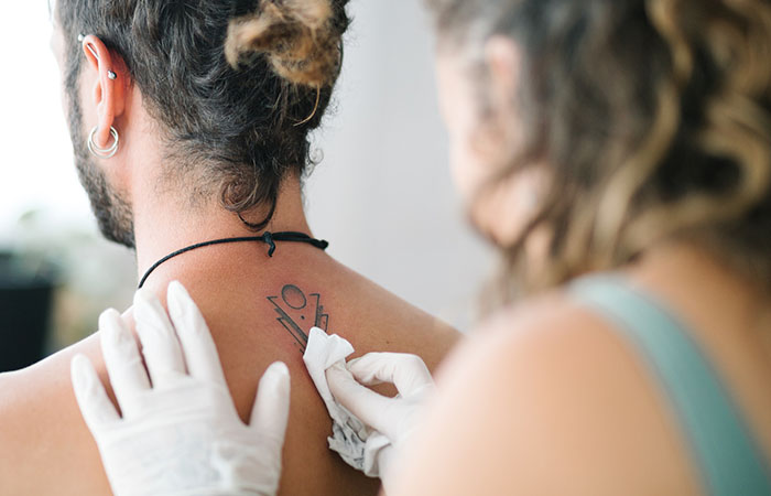 A tattoo artist uses a clean paper towel to wipe a fresh tattoo on the back of a client