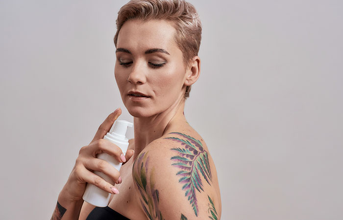 A woman applying a moisturizer on her beautiful watercolor-inspired tattoos over her shoulder