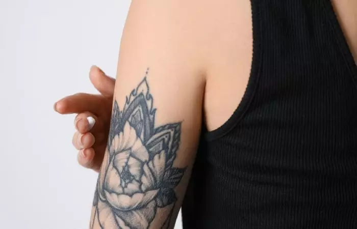 An individual applying Lubriderm unscented lotion on a tattoo at the back of the upper arm.