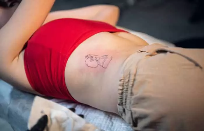 An individual lying down on a bed with a fresh tattoo on one side of their abdomen.