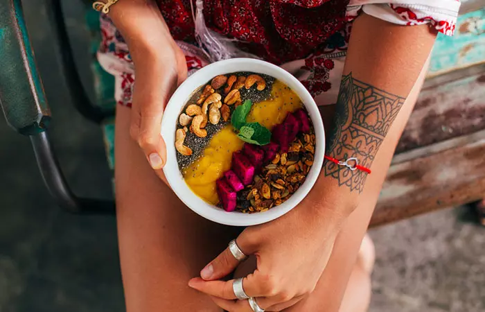 A tattooed girl with a healthy fruit bowl on her lap