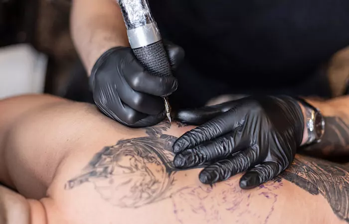Tattoo artist inks black color to the design