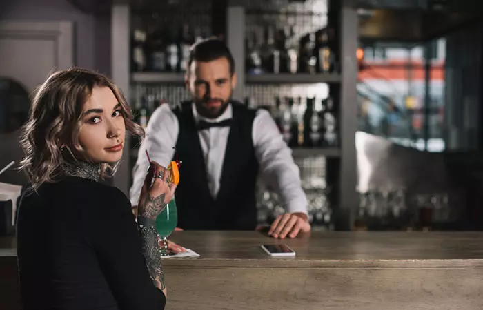 A tattooed girl with a drink at bar counter