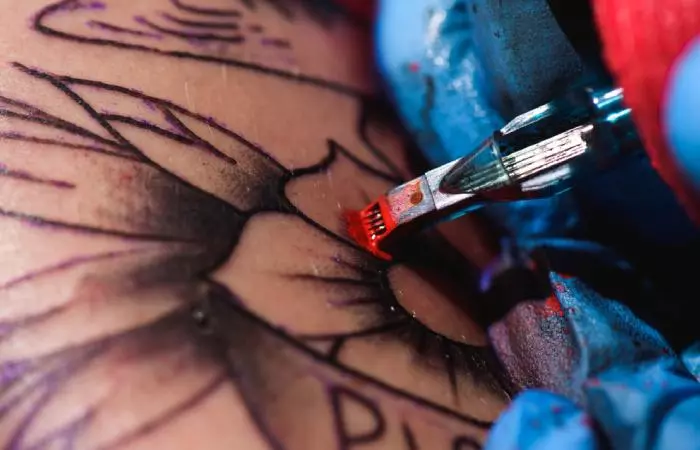 Close up of tattoo needles depositing red ink on the skin