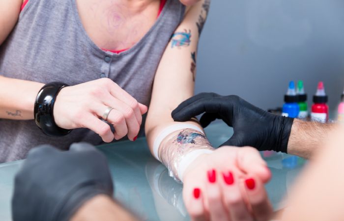 Close-up of the hand of a tattoo artist wrapping the forearm of a tattooed client with Saniderm