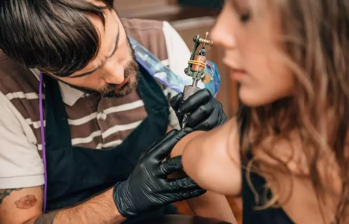 Tattooist working on woman's elbow