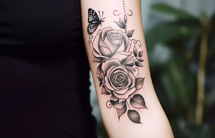A black rose and butterfly tattoo on the upper inner arm