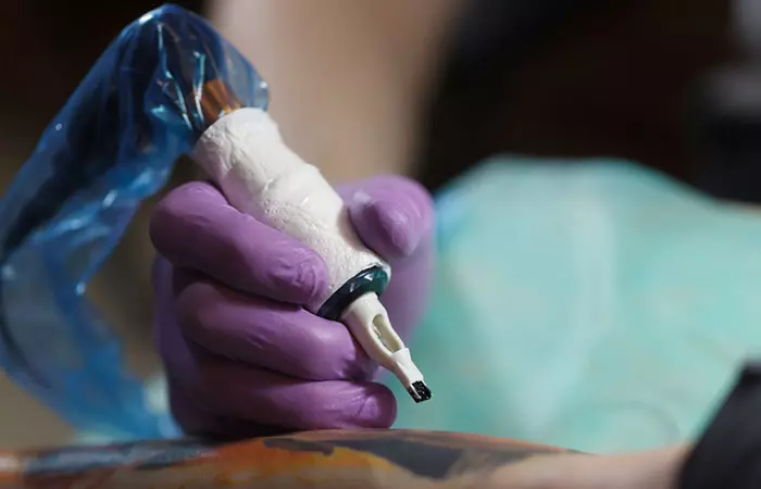 A tattoo artist holds a tattoo machine on their client’s arm