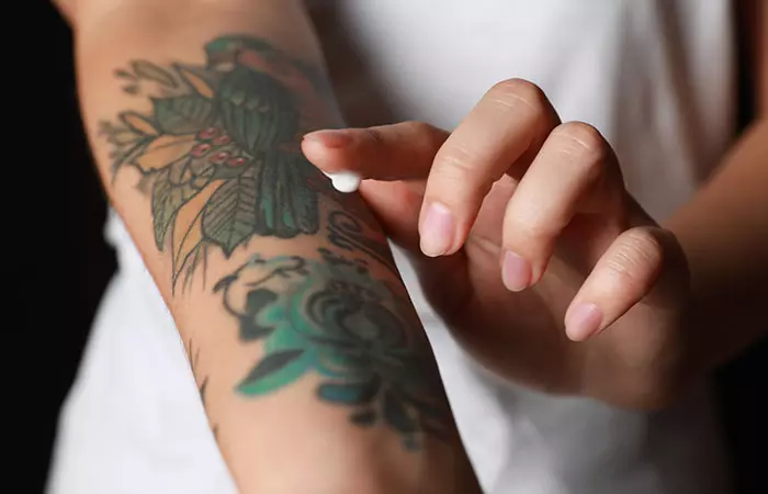 Woman applying ointment on her arm with tattoos