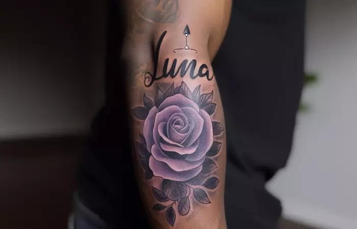 The name Luna tattooed in cursive above the rose on the arm