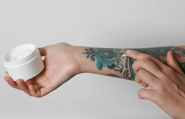 Woman applying cream on her arm with tattoos