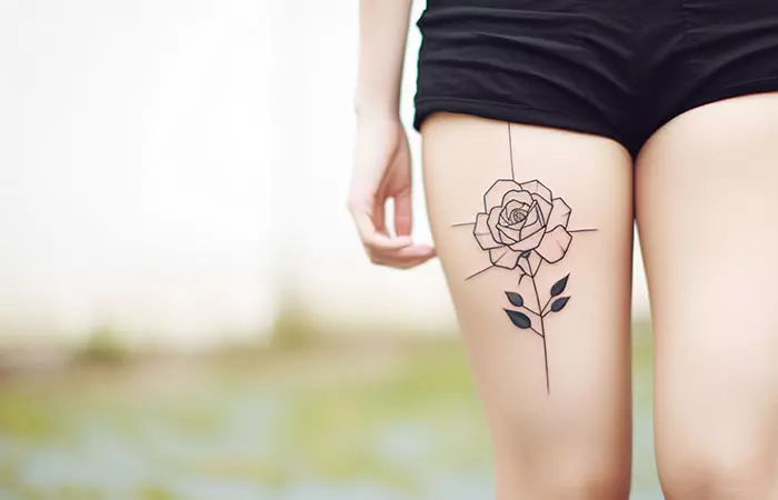 A discreet fine line minimal black rose tattoo on a woman’s thigh