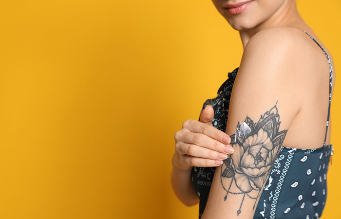 Woman applies Aveeno lotion to her floral tattoo on the back of her upper arm