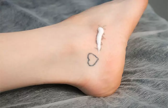 Woman applying cream on her foot with tattoo