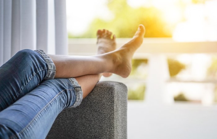 Woman lies on a sofa with legs elevated on the armrest.