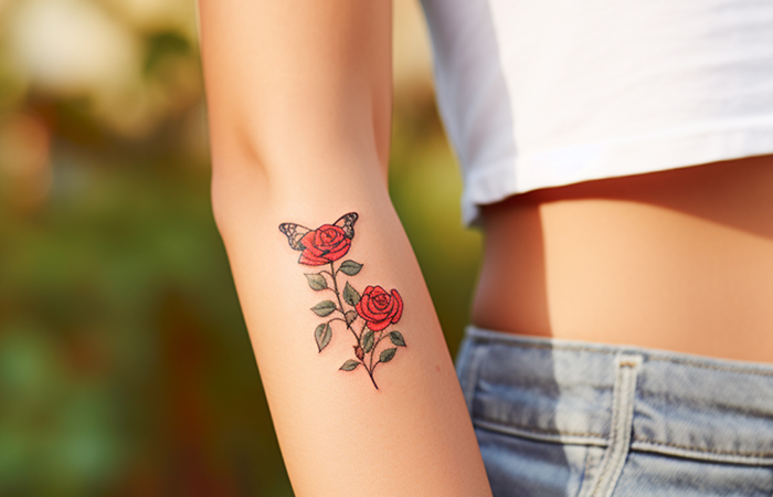A butterfly and red rose tattoo on the forearm of a woman