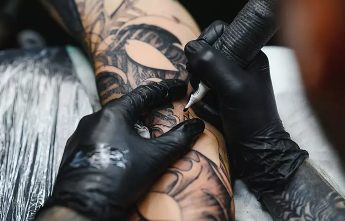 A close-up of a tattoo artist working on a blackout tattoo
