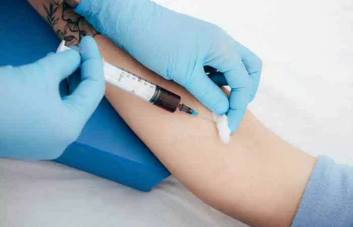 A doctor taking a blood sample from a tattooed arm