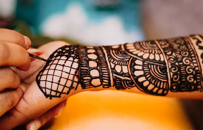 A henna artist creating a henna tattoo on a woman’s clean hands
