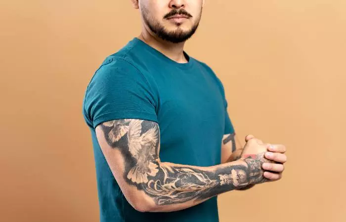 A muscular man shows off a full sleeve tattoo on one of his arms.