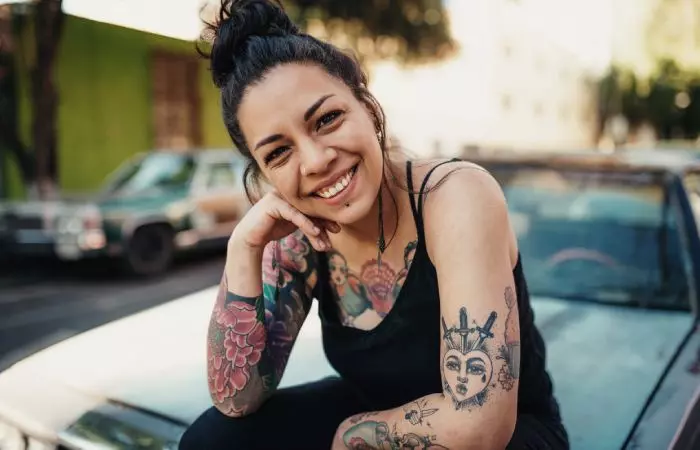 A smiling woman with multiple colorful and blackwork tattoos all over her arms and chest