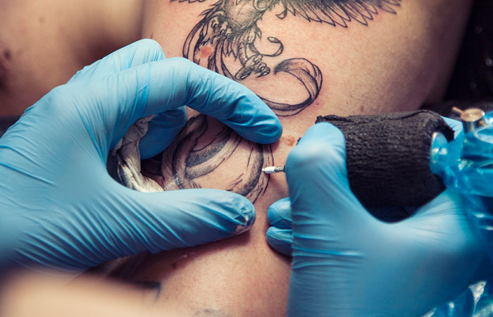 A tattoo artist creating a tattoo around the moles on their client’s arm