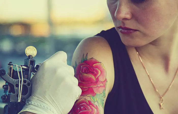 A tattoo artist draws a rose tattoo on a woman’s arm