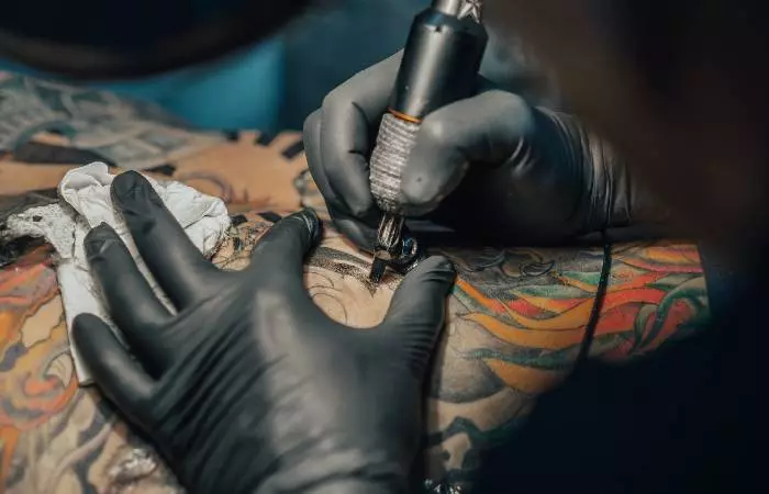A tattoo artist in black gloves tattooing on their client’s body