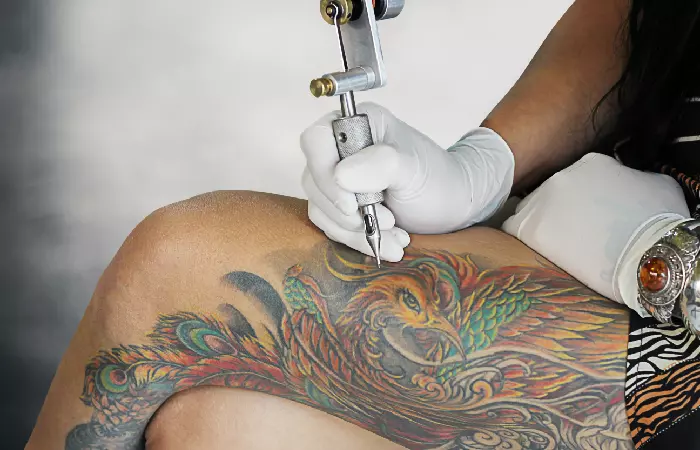 A tattoo artist inking a colored tattoo on dark skin