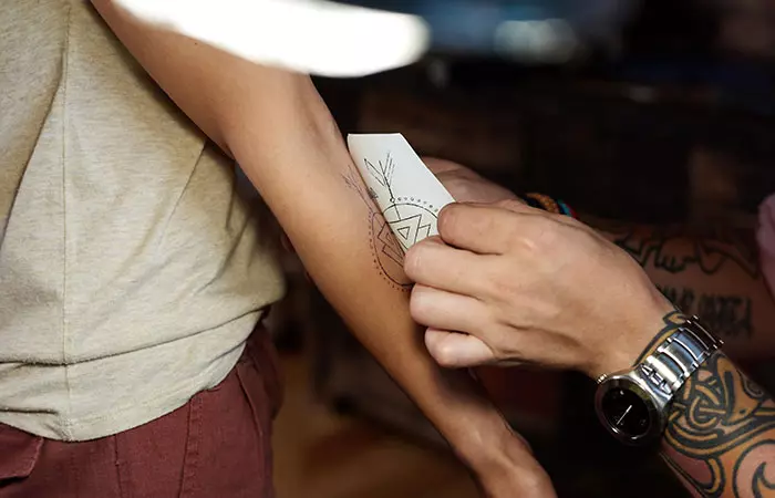 A tattoo artist transferring a tattoo image onto the hand of his customer from a piece of paper
