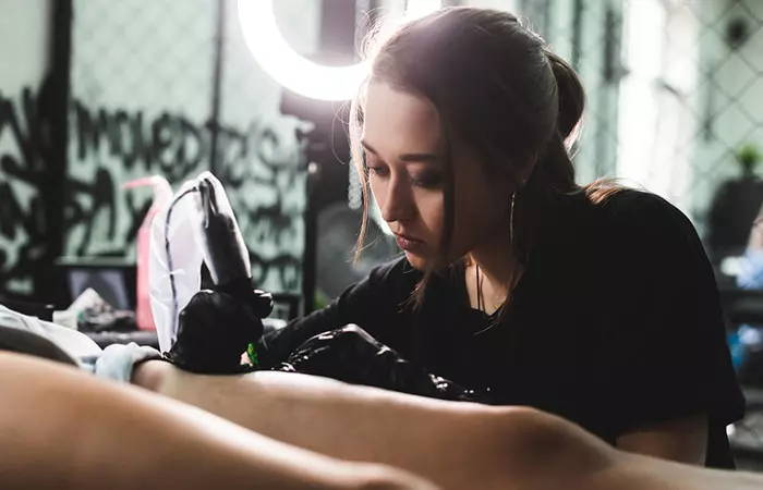 A tattoo artist working on her client’s arms