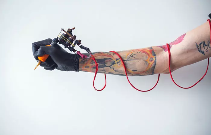 A tattooed hand holding a tattoo machine