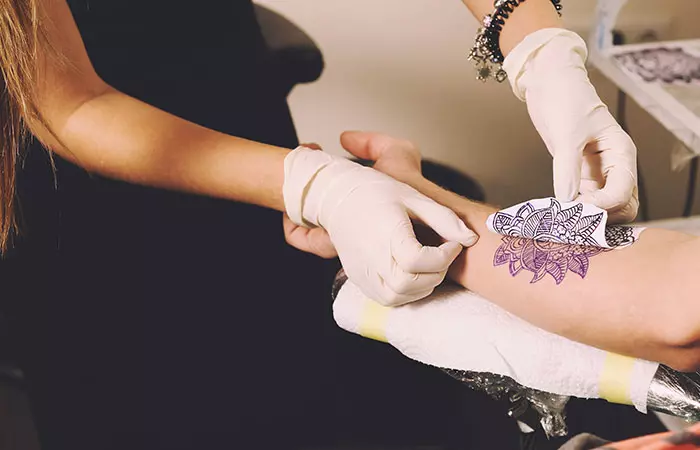 A tattooist transfers a tattoo sketch on a hand using thermographic transfer paper