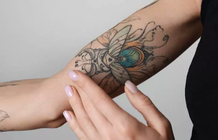 A woman applying moisturizer to her colorful tattoo