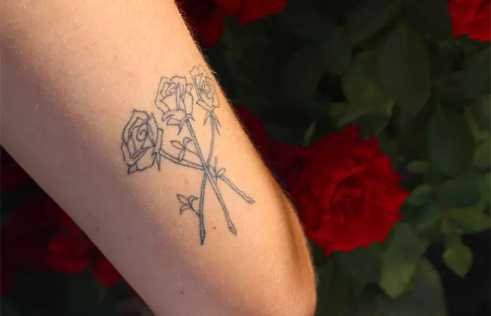 A woman sports a 3x3 tattoo with three roses on the back of her upper arm